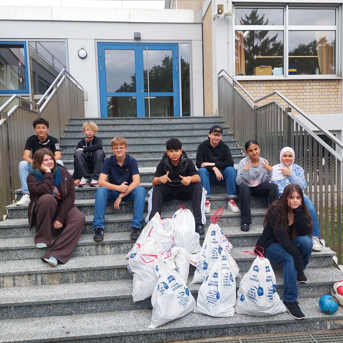 Schüler sitzen mit vollen Müllsäcken auf einer Treppe