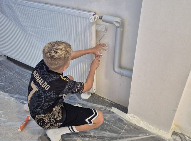 Ein Schüler rollt mit einer Farbrolle eine Wand