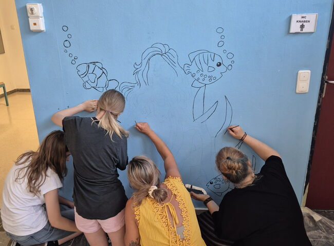 Schüler und Pädagogen bemalen zusammen eine Wand